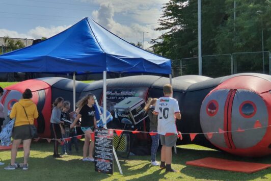 Children gather outside an inflatable laser tag arena with a blue canopy tent.