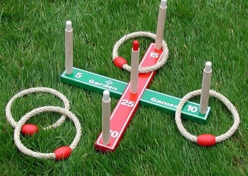 A quoits game set on grass with rope rings around wooden pegs on a colored scoring board.