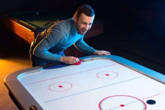 A man plays air hockey on a white table in a dimly lit room.