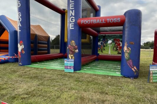 Inflatable football field goal and toss game set up outdoors on grass.