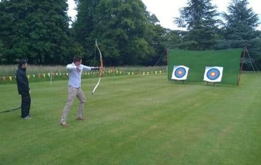 Two people practicing archery outdoors with two target boards on a grassy field.