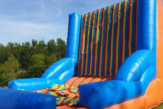 Inflatable Velcro wall game with bright stripes and a velcro suit lying on top, set outdoors.