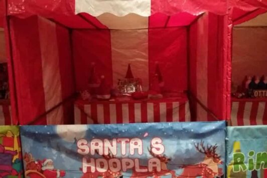 Red and white striped Christmas fair stall with a sign reading "Santa's Hoopla."