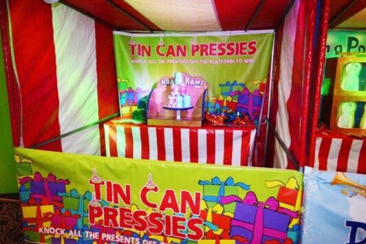 A Christmas fun fair stall named "Tin Can Pressies" with colorful presents and a striped booth.