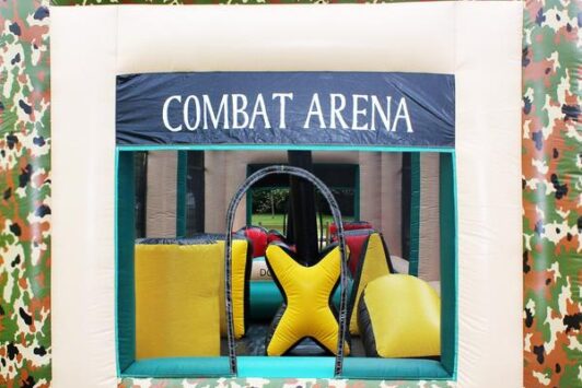 Inflatable combat arena with camouflage pattern and yellow obstacles on grass.