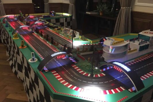 A digital slot car racing track set up indoors with lights and detailed scenery.