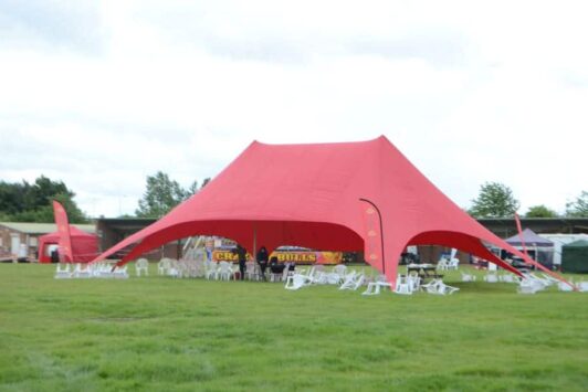 Large red event tent with chairs on a grassy field at an outdoor festival.