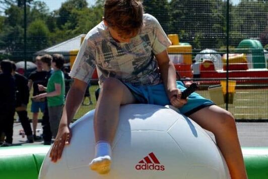 Boy riding a large inflatable football outdoors at an event.