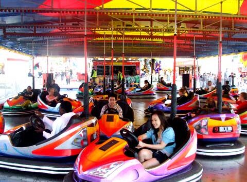 People riding colorful bumper cars at a funfair under a bright yellow and red canopy.