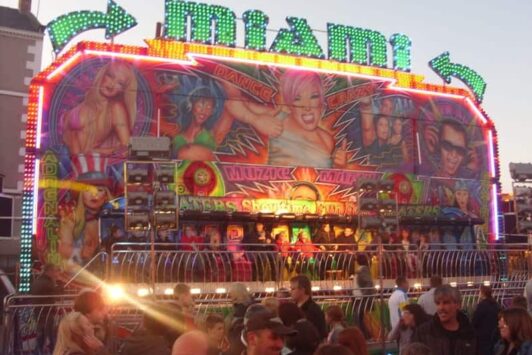 Colorful Miami fairground ride with bright lights, artwork, and people gathered in front.