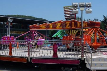 Colorful Sizzler fairground ride with people spinning on bright seats at an outdoor fair.