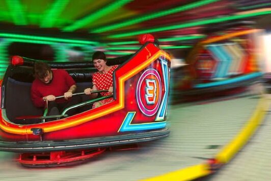 Two people enjoying a colorful spinning waltzer ride at a fun fair.