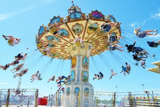 People riding a colorful wave swinger ride at an outdoor fair under a clear blue sky.