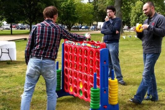 Three people playing a giant Connect Four game outdoors on grass.