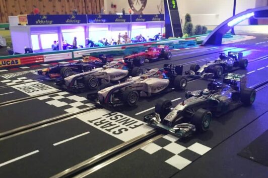 Model Formula 1 cars lined up on a slot car racing track at the start/finish line.