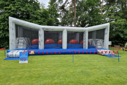 Inflatable obstacle course with large red balls on a grassy field.