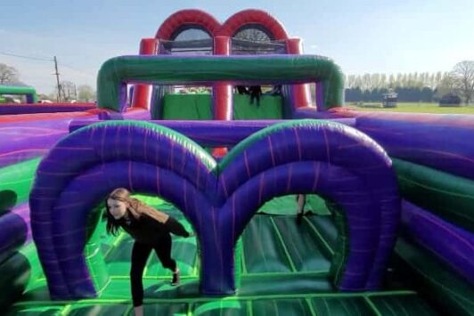Person crawling through a colorful inflatable obstacle course outdoors on a sunny day.