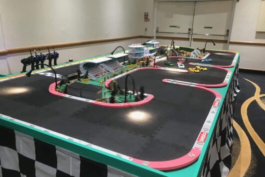 A model race track with remote-controlled cars and controllers on a checkered table.