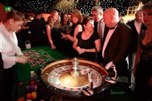 People playing roulette at a casino table under decorative lights.