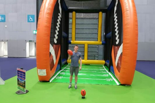 Man stands in front of an inflatable rugby conversion challenge game holding a rugby ball.