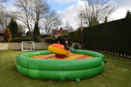 Person riding an inflatable rugby simulator in a backyard with grass and trees.