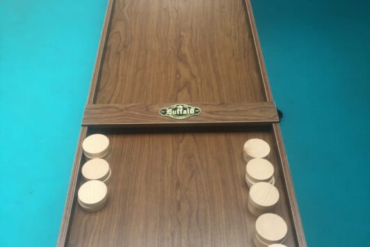 Wooden shuffleboard game with round pucks on a brown table and a blue floor background.
