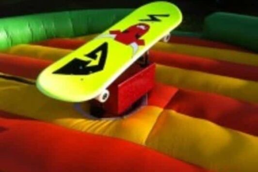 A yellow skateboard simulator on an inflatable red and yellow mat.