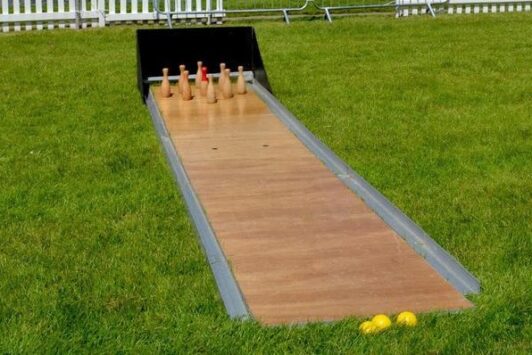 Skittle alley set up outdoors on grass, with wooden pins and yellow balls ready to play.