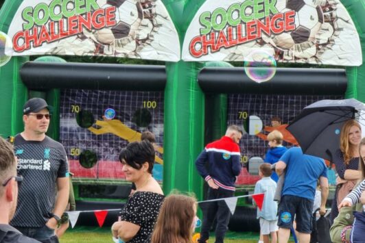 People gathered in front of inflatable soccer challenge games at an outdoor event.