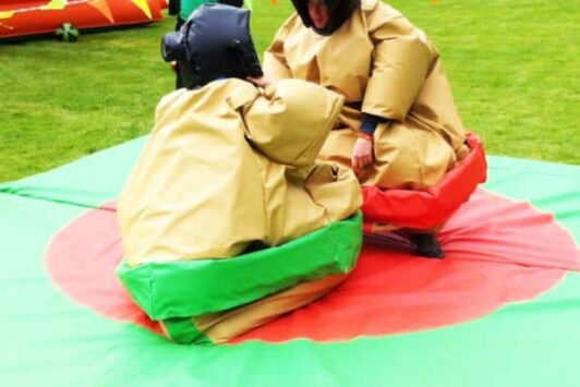 Two people in sumo suits face each other on a mat outdoors, ready to wrestle.
