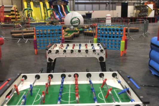 Table football and giant Connect Four games set up in an indoor play area with inflatables in the background.