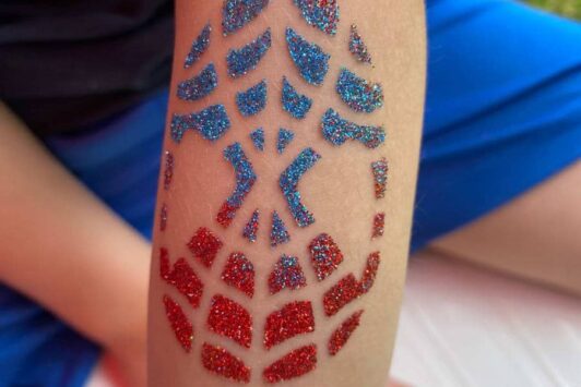 Red and blue glitter temporary tattoo in a geometric pattern on a child's arm.