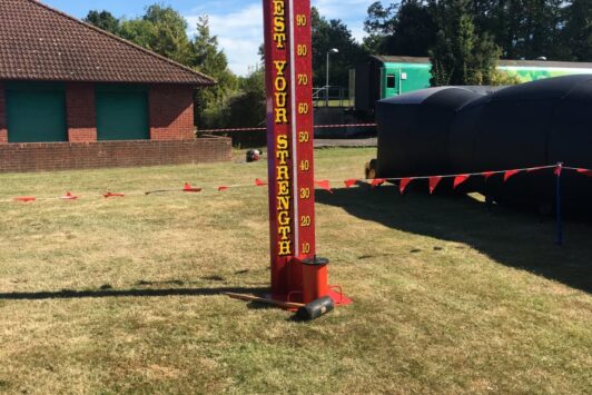 Red "Test Your Strength" carnival game stands on grass under a blue sky.