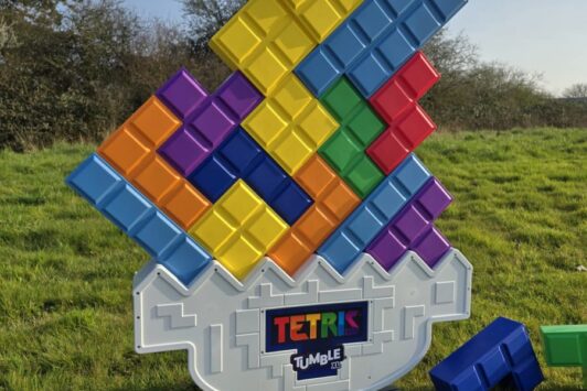 Large colorful Tetris Tumble XL game setup outdoors on grass, with pieces and a die nearby.