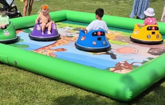 Four toddlers ride colorful bumper cars in an inflatable play area with animal designs on the mat.