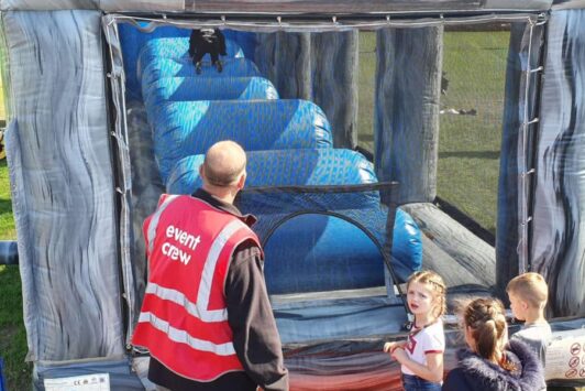 Children line up at an inflatable obstacle course with an event crew member supervising.